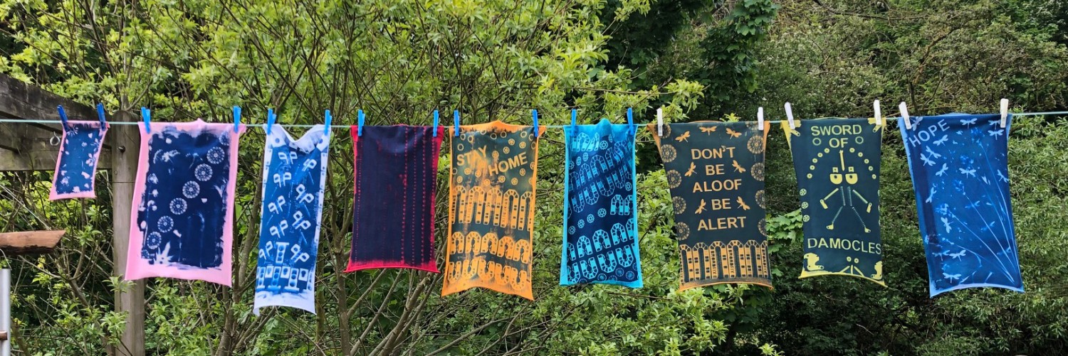 Prints in a variety of bright colours hung on a washing line with green trees in the background